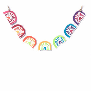 7 Colourful Rainbows are sewn together to create an adorable little garland, displayed against a white background