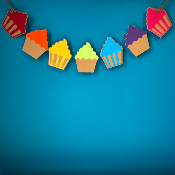 A string of 7 cupcakes is shown hanging against a blue wall.