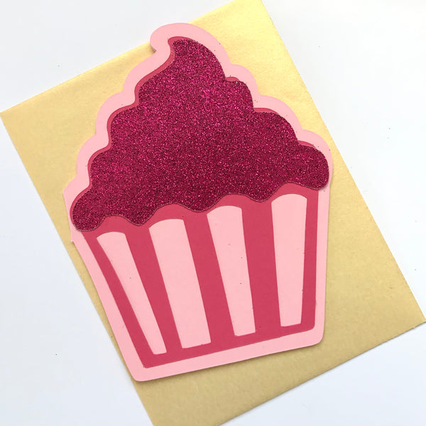 a cupcake shaped card in shades of pink is shown paired with a gold envelope against a white background