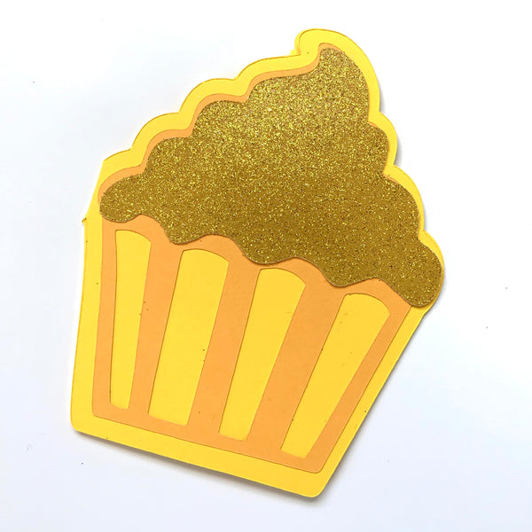 A yellow cupcake shaped card with glittery gold frosting is shown on a white background