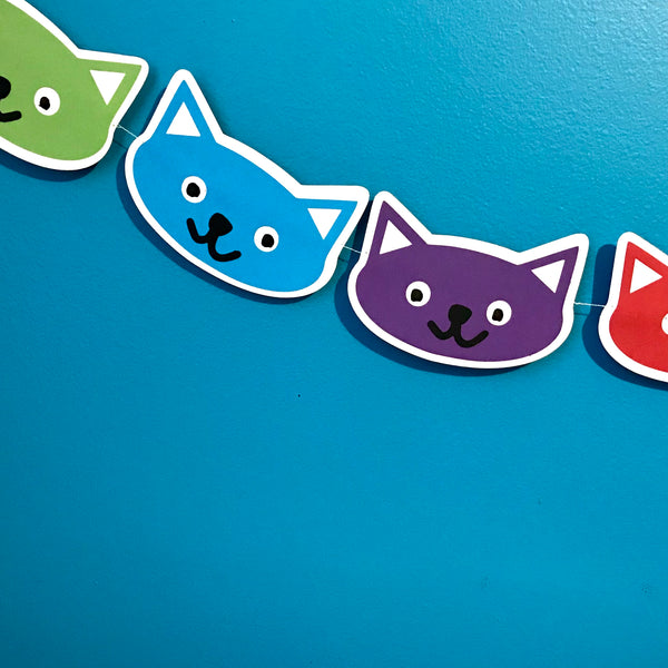 a portion of a cat head garland is shown against a blue background.  Two full cat heads, in blue and purple, are shown with 2 partial cat heads in green and red.