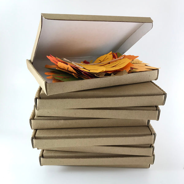 A stack of small brown boxes is shown on a white background.  The top box is open, and shows a small pile of paper leaves in fall colours.