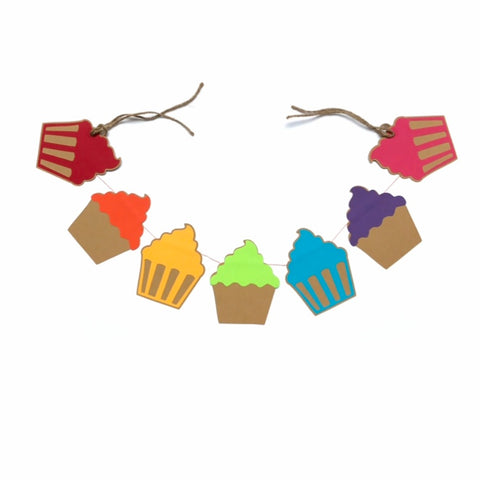 A little garland of 7 cupcakes is shown against a white background.  There is hemp cord on either end of the banner.  Each cupcake is a different colour of red, orange, yellow, green, blue, purple, pink