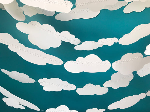 Dozens of white clouds are sewn into strings and hung against a blue background