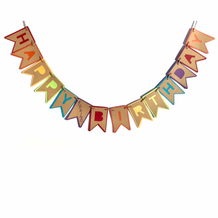 A banner that reads "happy Fucking birthday' is hung on a white background.  Each letter in Happy and Birthday is cut from brown cardstock and mounted onto colourful cardstock in a repeating rainbow pattern.  The word fucking is cut from one tab, hung between happy and birthday, for a subtle sweary effect.