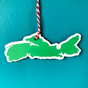 a paper gift tag in the shape of the province of Nova Scotia hangs from a red and white string against a blue background