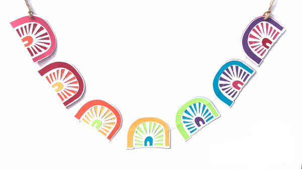 a paper garland with 7 little rainbows is shown against a white background.  Each rainbow is a different colour pattern.