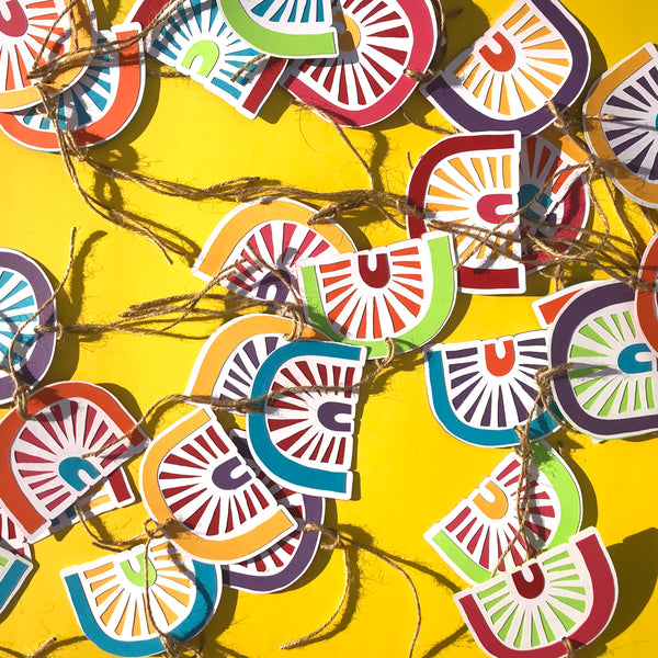 A scattering of paper rainbow gift tags are shown against a yellow background