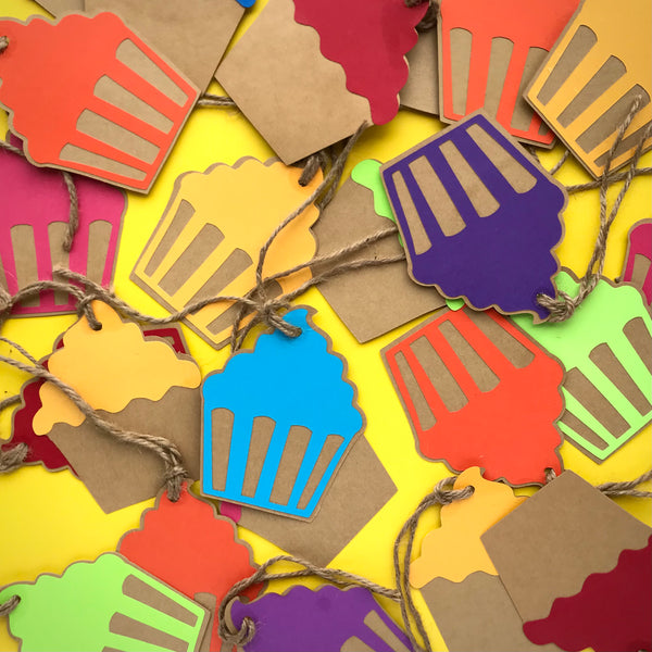 Dozens of colourful paper cupcake shaped gift tags are shown scattered across a bright yellow background