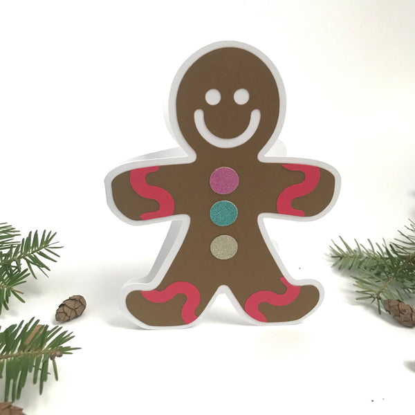A gingerbread man shaped card stands on a white background with ever green accents.