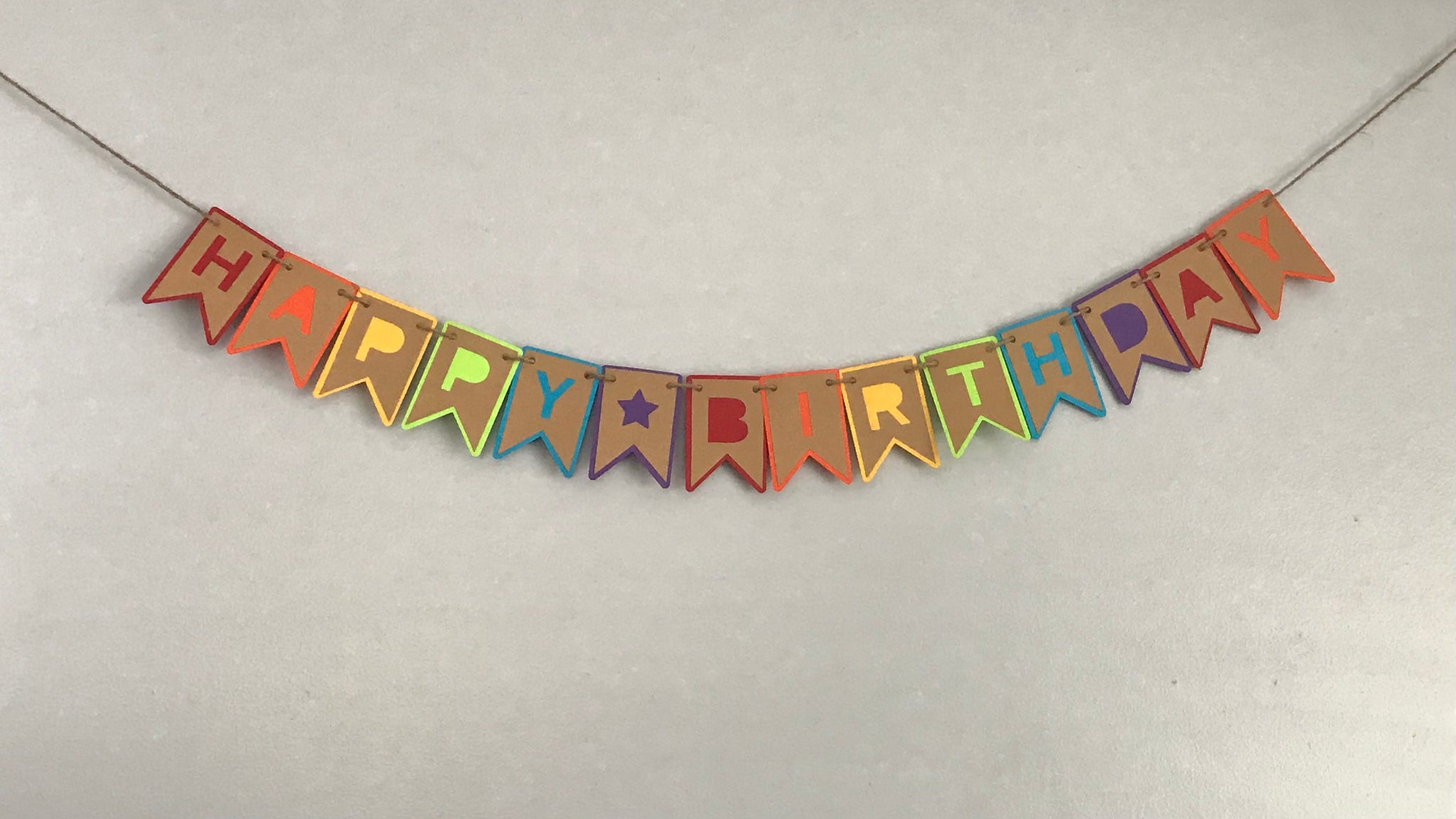 A happy Birthday banner is hung on hemp against a light grey background