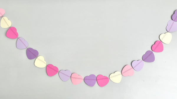 A long string of hearts in shades of pink, purples and creams is shown against a soft grey background.