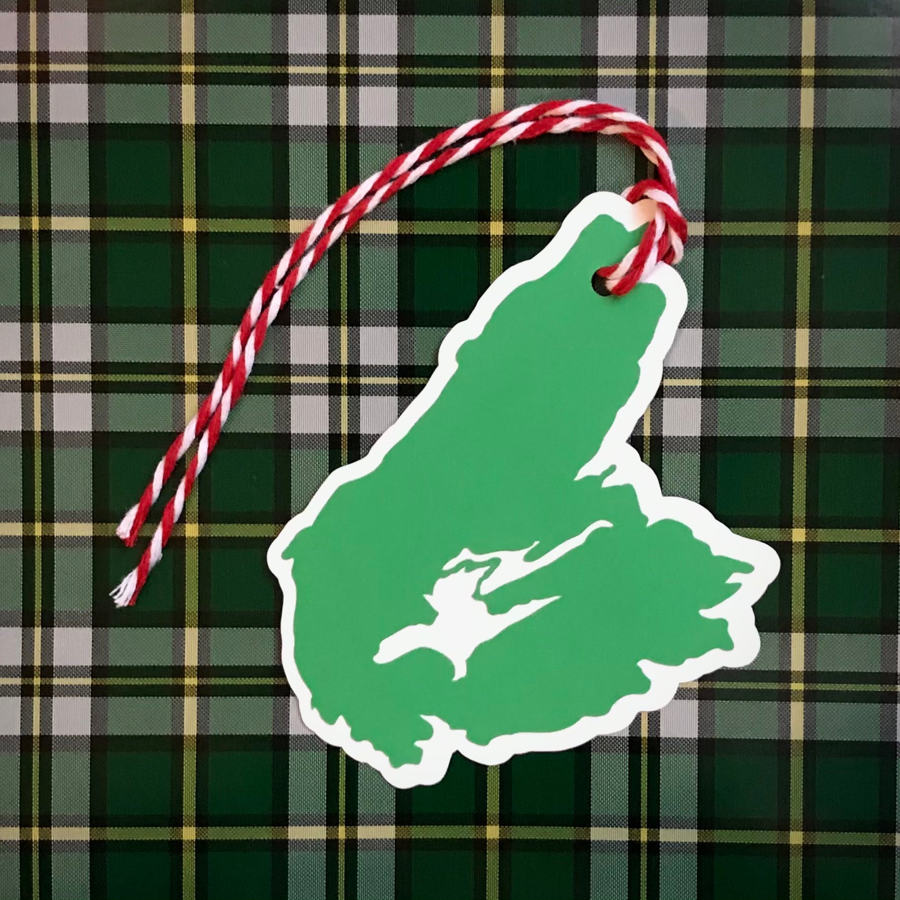 a paper gift tag in the shape of cape breton island is shown against a background of the official Cape Breton Island Tartan.