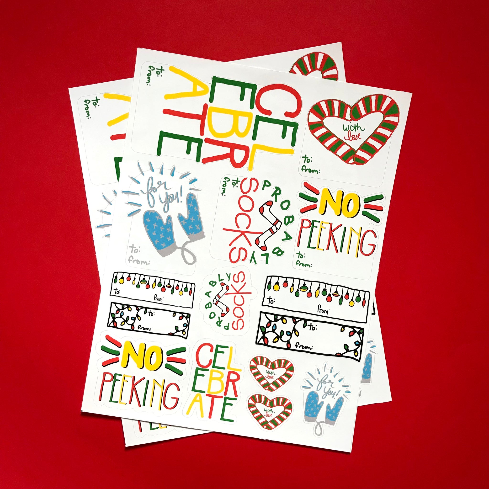 two sheets of festive sticker tags are displayed against a red background.  Phrases like CELEBRATE, FOR YOU and WITH LOVE are seen, among others