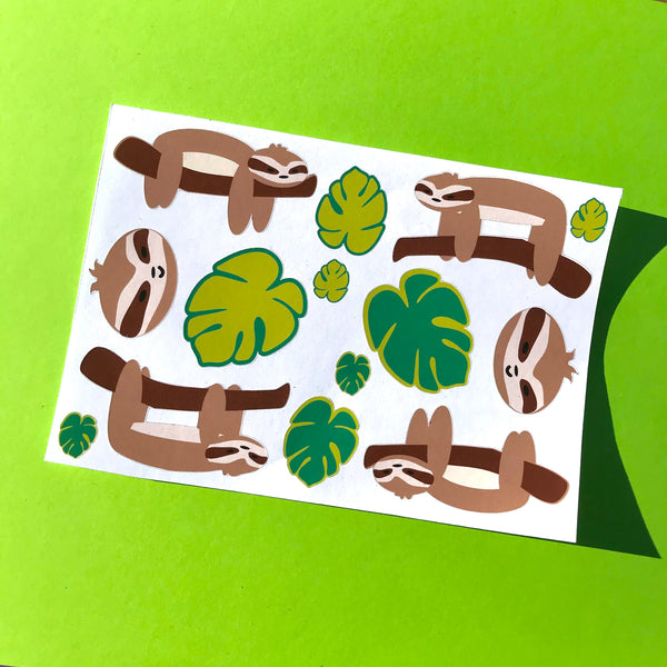 A single sheet of sloth and leaf stickers is shown against a bright green background