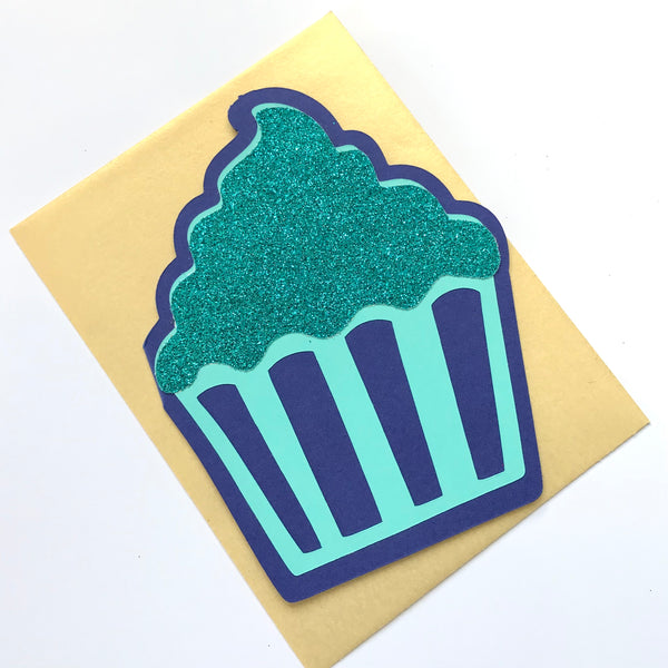 A cupcake shaped card in shades of blue is shown paired with a gold envelope against a white background