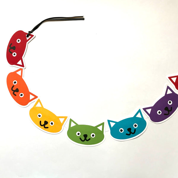 a portion of a cat head garland is shown displayed in a slight swooping curl against a white background.  there are 6 cat heads in total, coloured red, orange, yellow, green, blue and purple.  The garland is displayed going out of the image to the right implying it is bigger than the 6 cat heads.