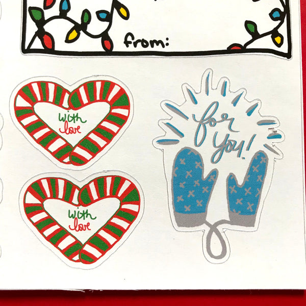 A close up image of some sticker tags.  Two look like little hearts made from candy canes with WITH LOVE in the center of the heart.  The third is a pair of blue mittens that appear to be holding the words FOR YOU!