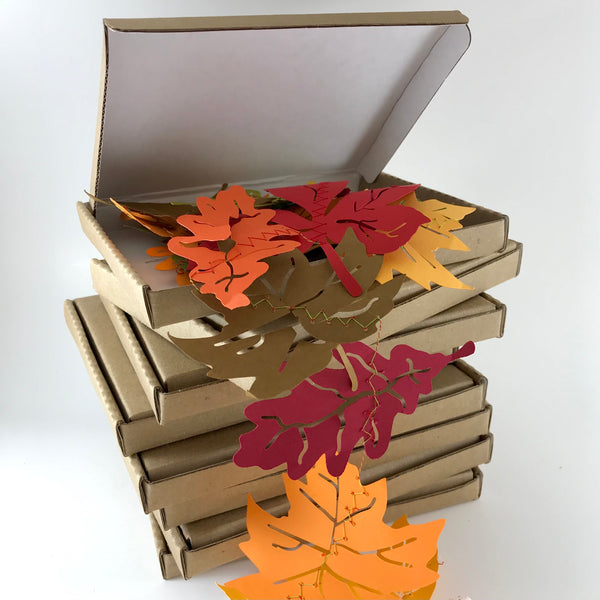 A small stack of brown boxes is shown on a white background.  The top box is open and a string of colourful fall leaves tumbles out