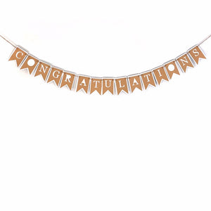 A banner that reads "CONGRATULATIONS" is hung against a white background.  Each letter in the word congratulations is cut from kraft brown paper, with white paper showing through the cut outs.  Each letter tab is hung on a hemp cord to create the finished piece