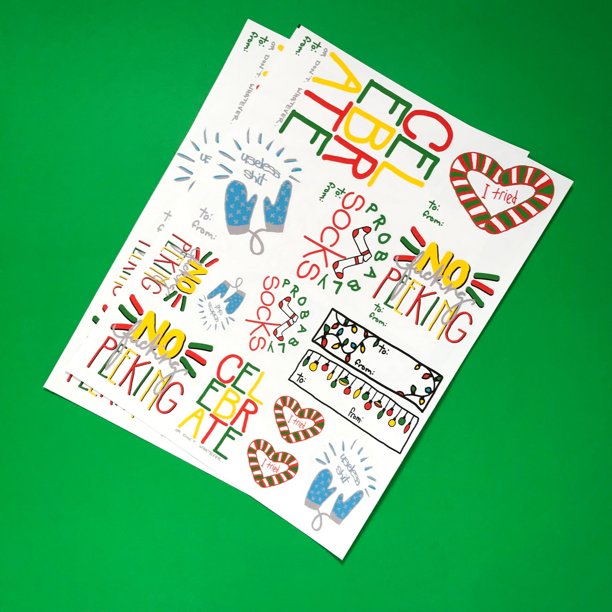 two sheets of holiday gift tag stickers are shown against a cheery green background.  The tags of funny adult humor sayings like no fucking peeking and useless shit